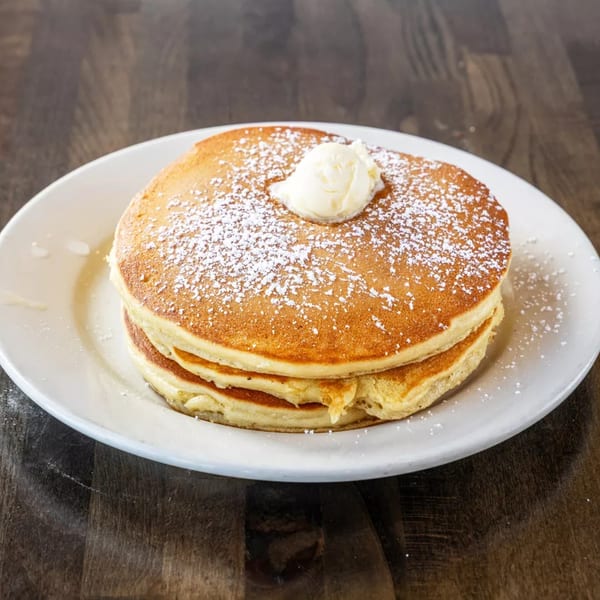 Stack of three golden pancakes with a dollop of butter and powdered sugar on a white plate.