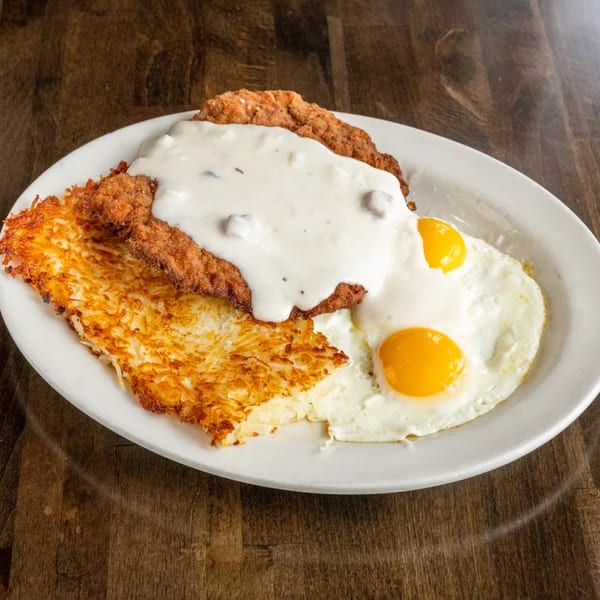Chicken fried steak with gravy, hash browns, and two fried eggs on a white plate.
