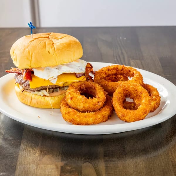 A cheeseburger with bacon and a fried egg, served with a side of crispy onion rings.
