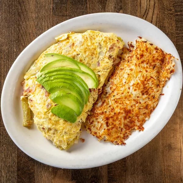 A breakfast plate with a golden-brown omelet topped with sliced avocado, and crispy hash browns.