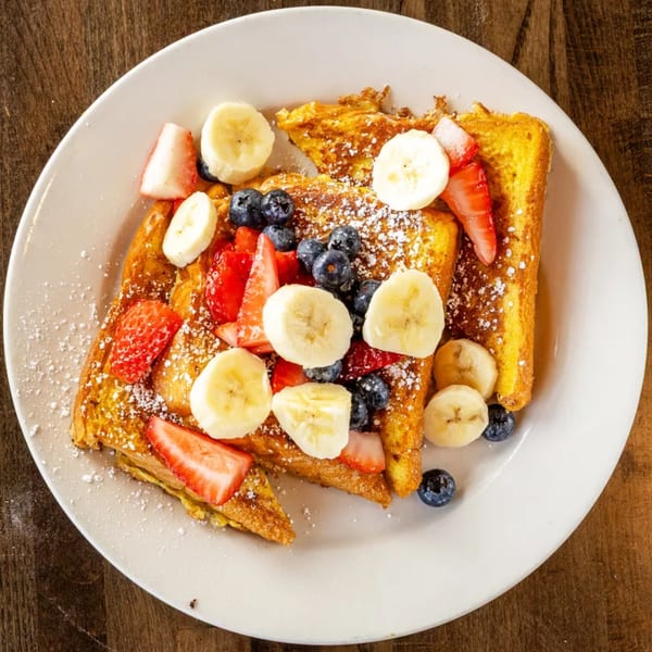 Golden French toast triangles on a white plate, topped with sliced bananas, blueberries, and strawberries.