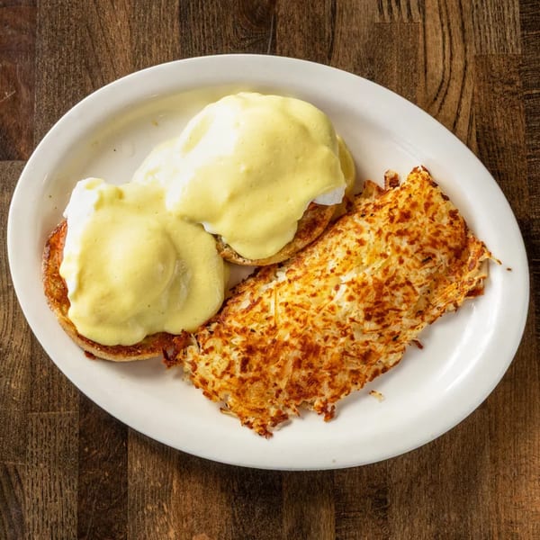 Eggs Benedict with hollandaise sauce and a side of crispy hash browns on a white plate.
