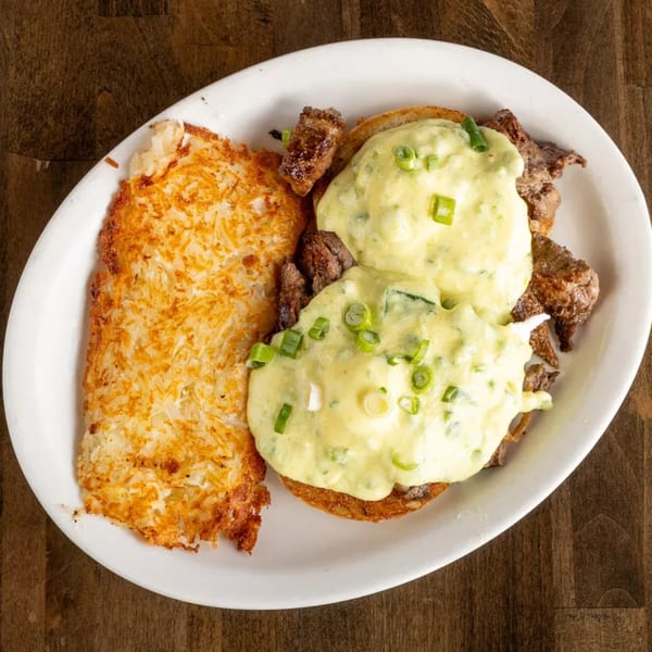 Steak Benedict with creamy green sauce and hash browns on a white plate.